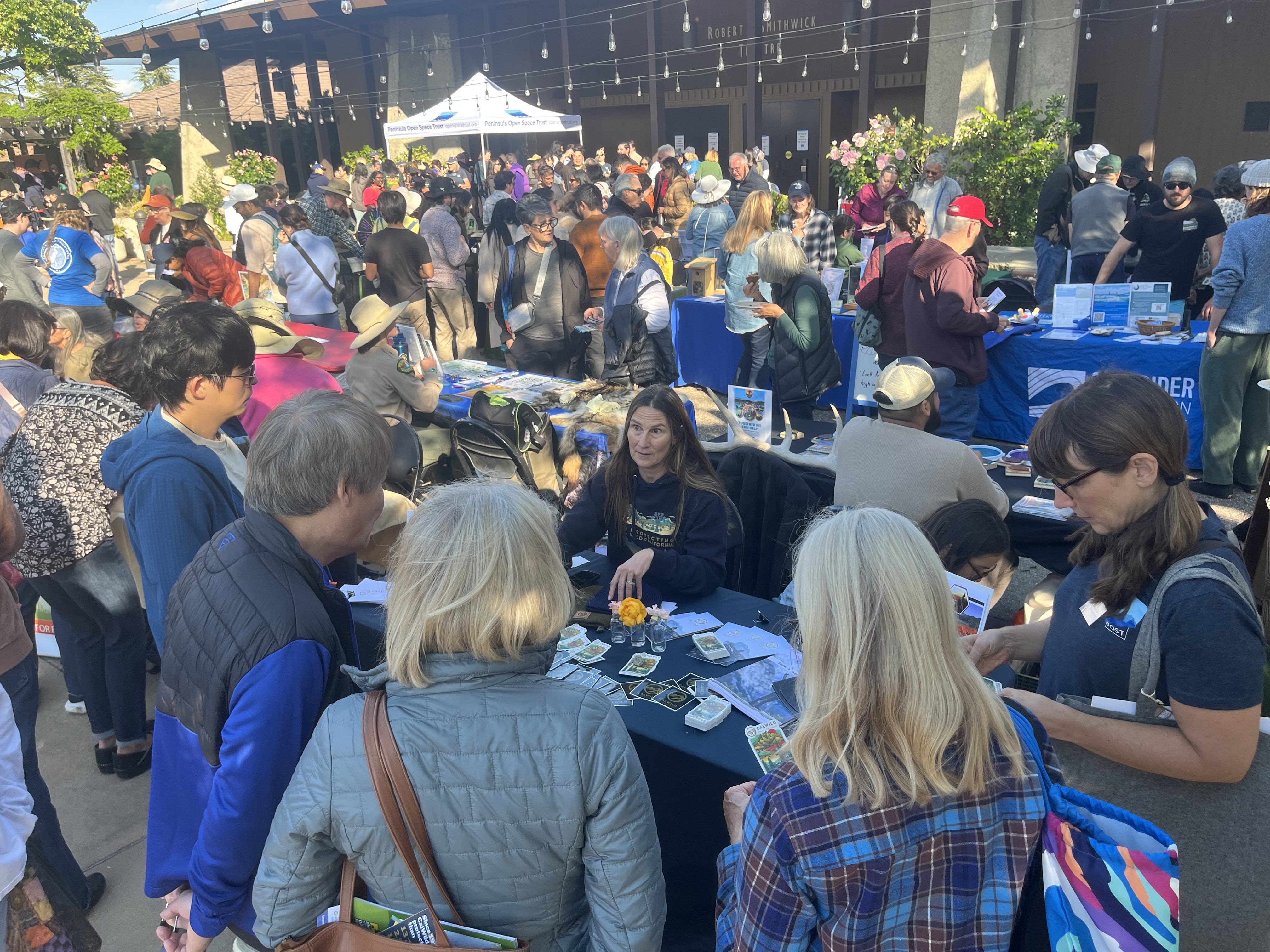 Community members gathered at a Coastside outdoor event, talking with volunteers at information tables